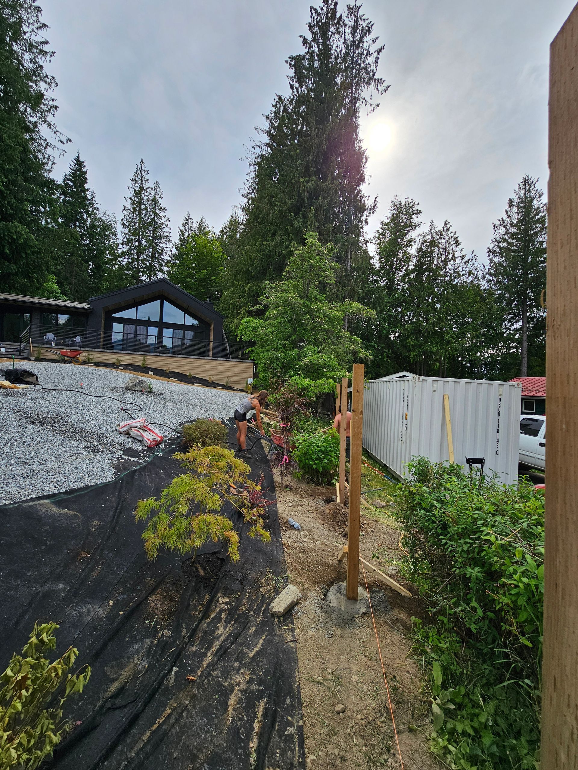 Fence post set in concrete on a rocky hillside path, with a house and trees in the background.