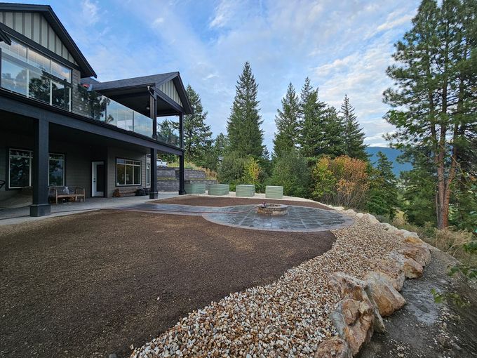 House with deck overlooking a fire pit and surrounding hillside, with trees against a cloudy sky.
