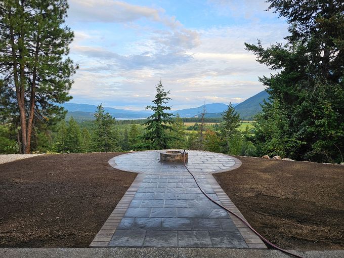 Stone patio with fire pit, overlooking a valley with mountains under a cloudy sky.