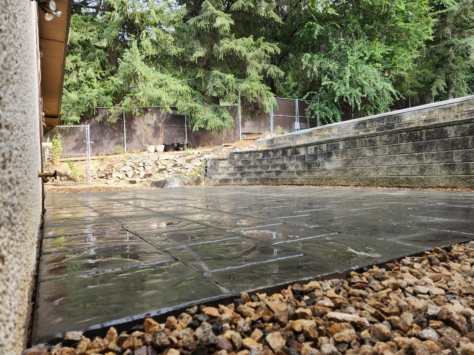 A patio with gravel and a stone wall in the background.