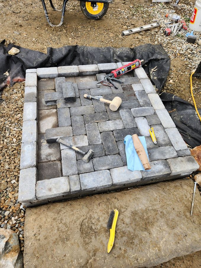 Square brick patio under construction, gray pavers and tools on soil.