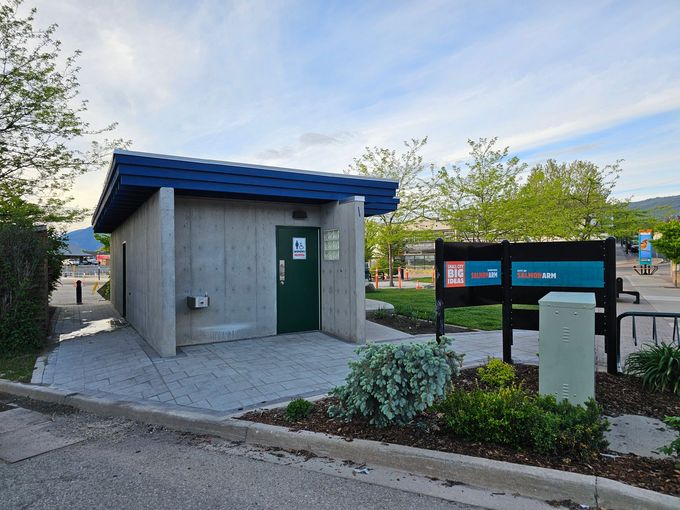 Concrete public restroom with a green door and blue roof, in a park setting.