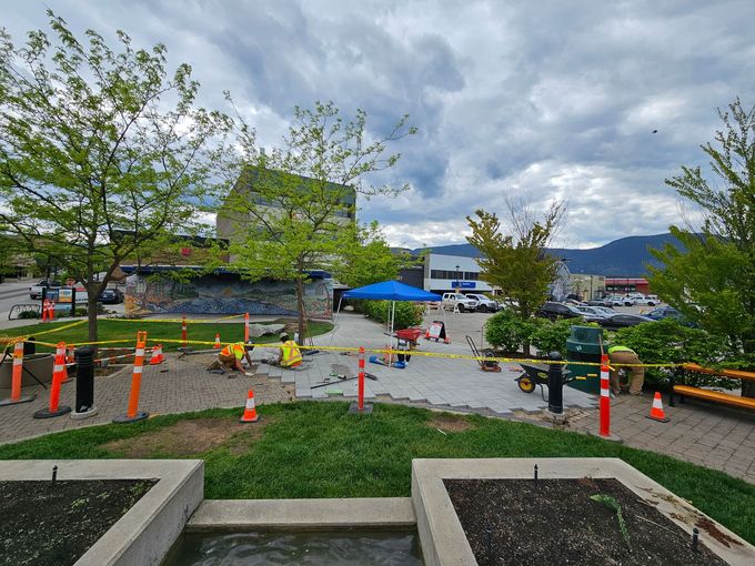 Workers and equipment around a construction area; green trees, grey sky.