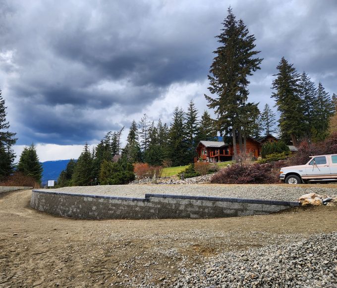 Gravel driveway with retaining wall, house in the background, overcast sky, truck parked.
