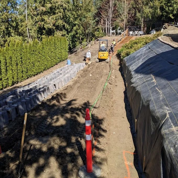 Construction site with a small excavator, workers, and retaining walls.