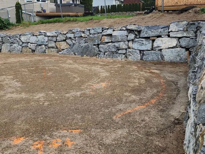Stone retaining wall framing a gravel-covered area, potentially for a driveway or patio.