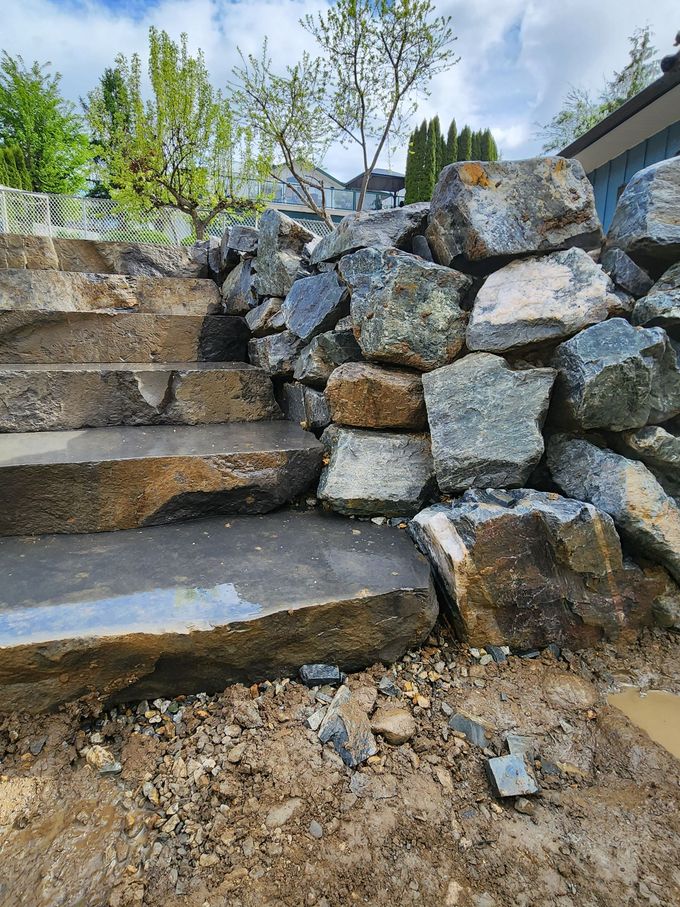Stone steps alongside a rock retaining wall, outdoors. Construction debris visible.