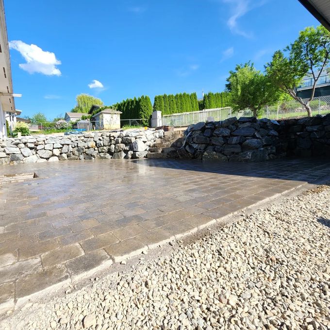 A wet concrete patio with rock borders under a bright blue sky.