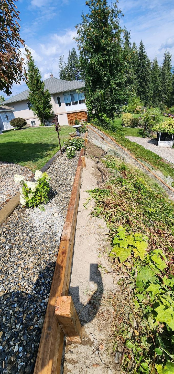 A residential yard with a wooden planter box and a dirt path next to a house.