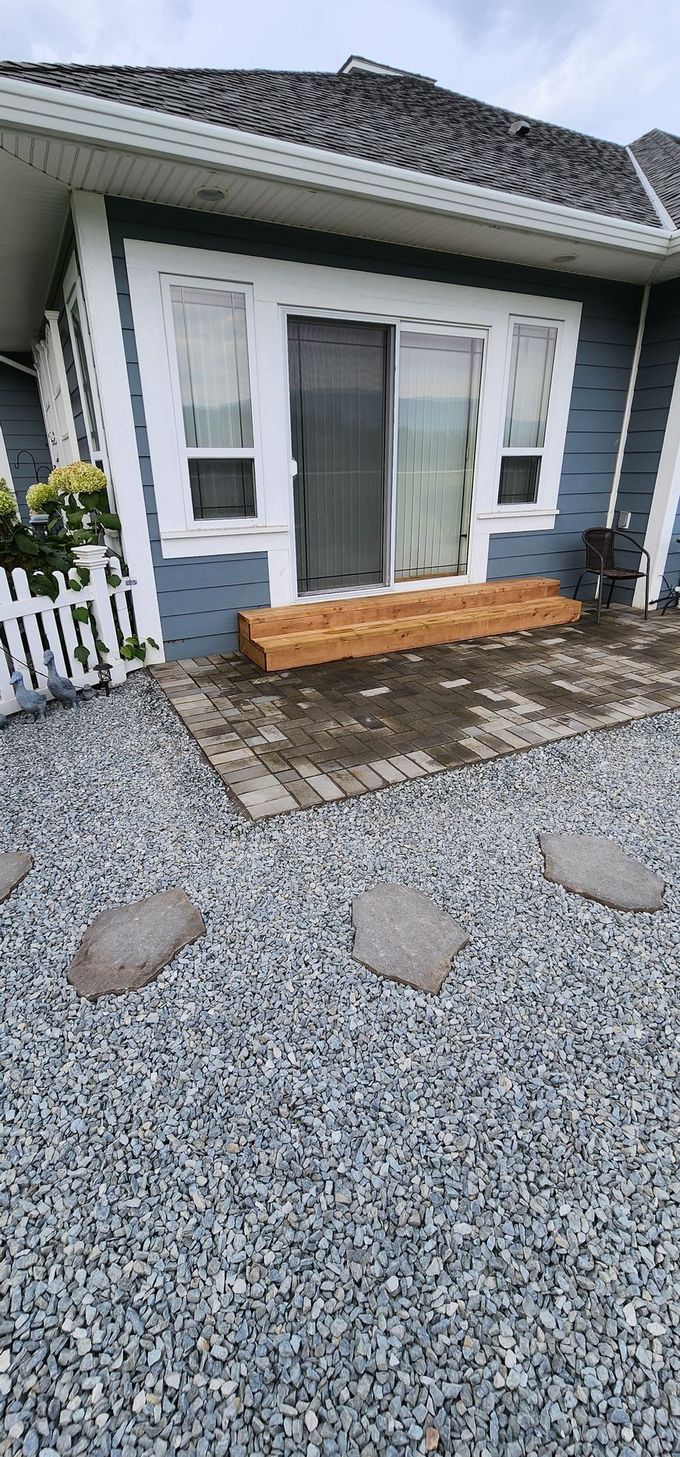 Blue house with wooden deck and gravel yard with stepping stones.