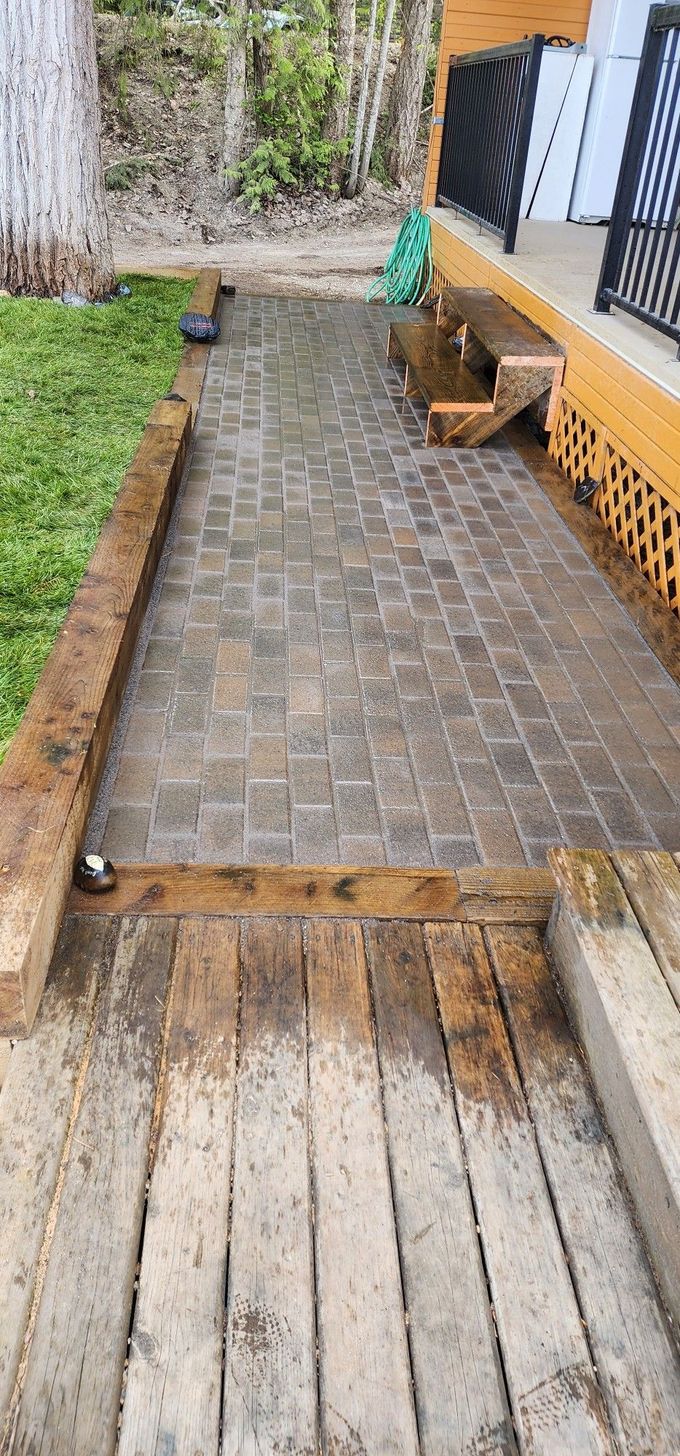 Wooden deck, brick path, and grassy area leading to a building with black railings.