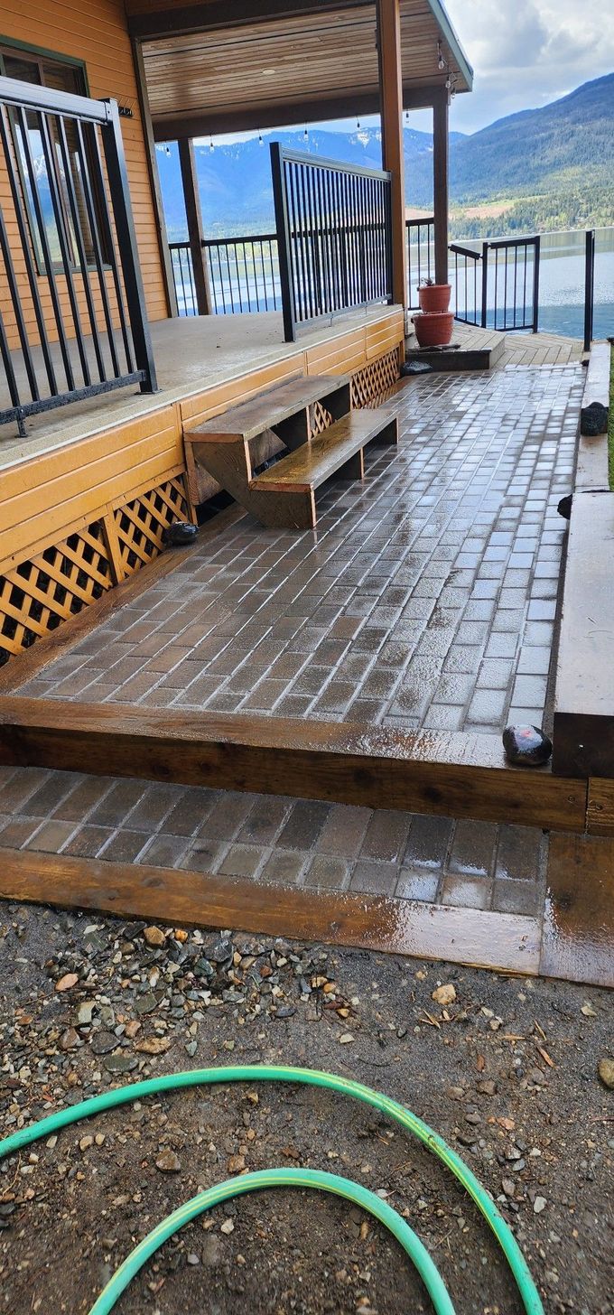 Wooden deck and brick patio with steps, view of mountains and water in the background.