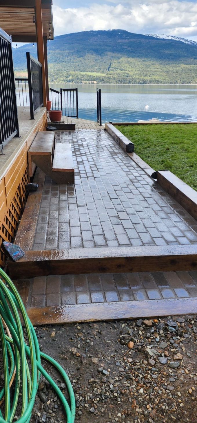 Brick patio with a view of a lake and mountains. A green hose is in the foreground.