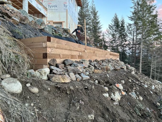 A person building a wooden retaining wall on a hillside next to a house.