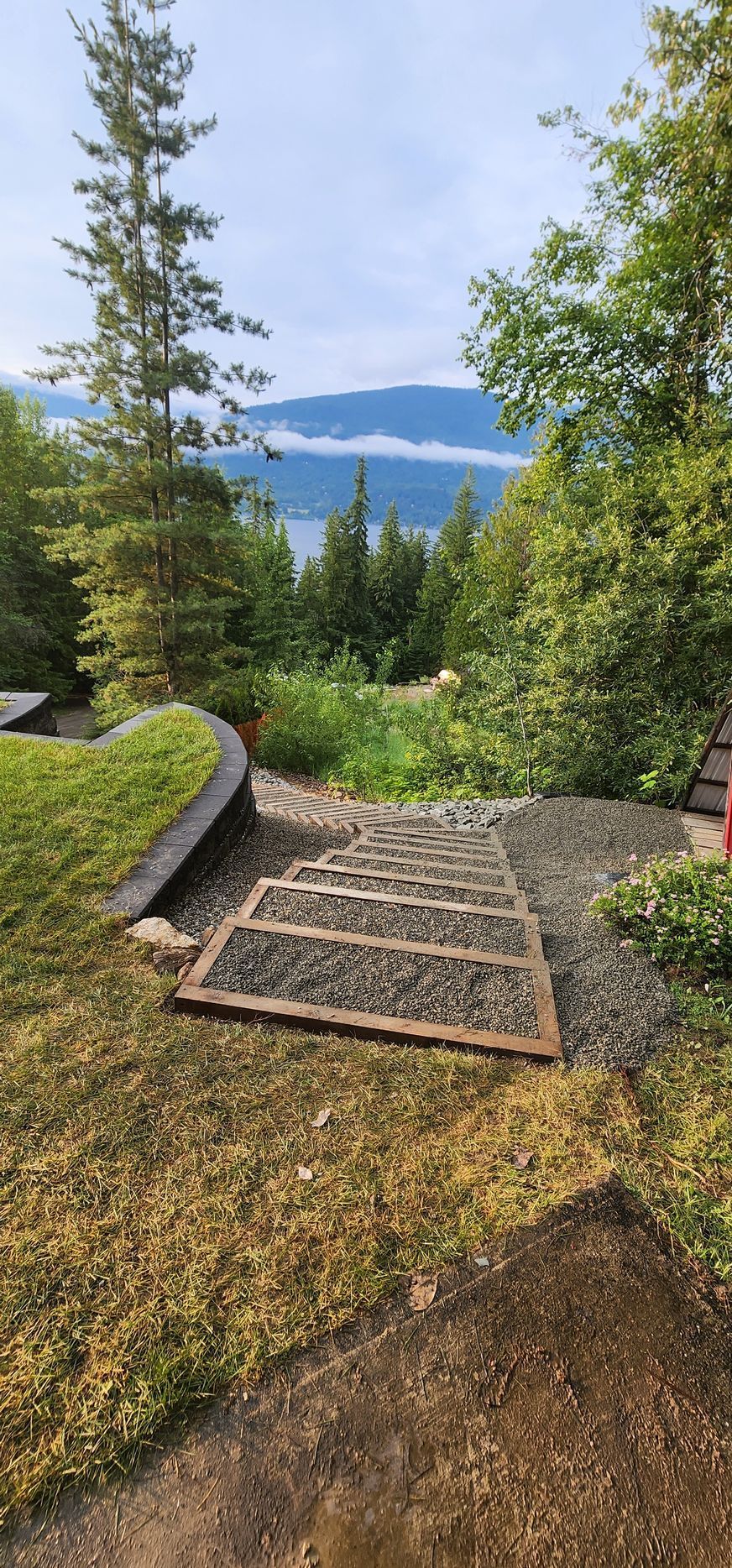 Stone steps lead to a scenic view of a lake and mountains, surrounded by trees and greenery.