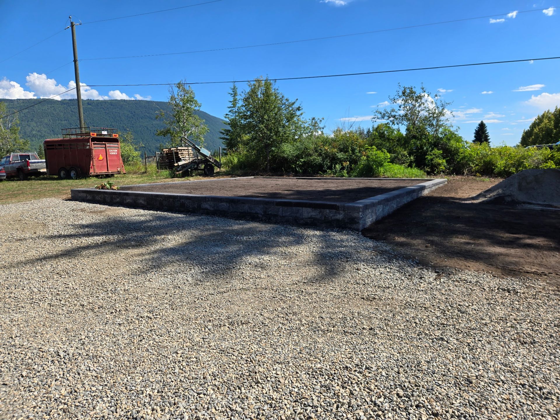Gray concrete platform on gravel, with trees, a red box, and mountains in background.