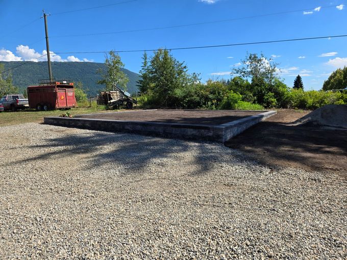 Gray concrete platform on gravel, with trees, a red box, and mountains in background.