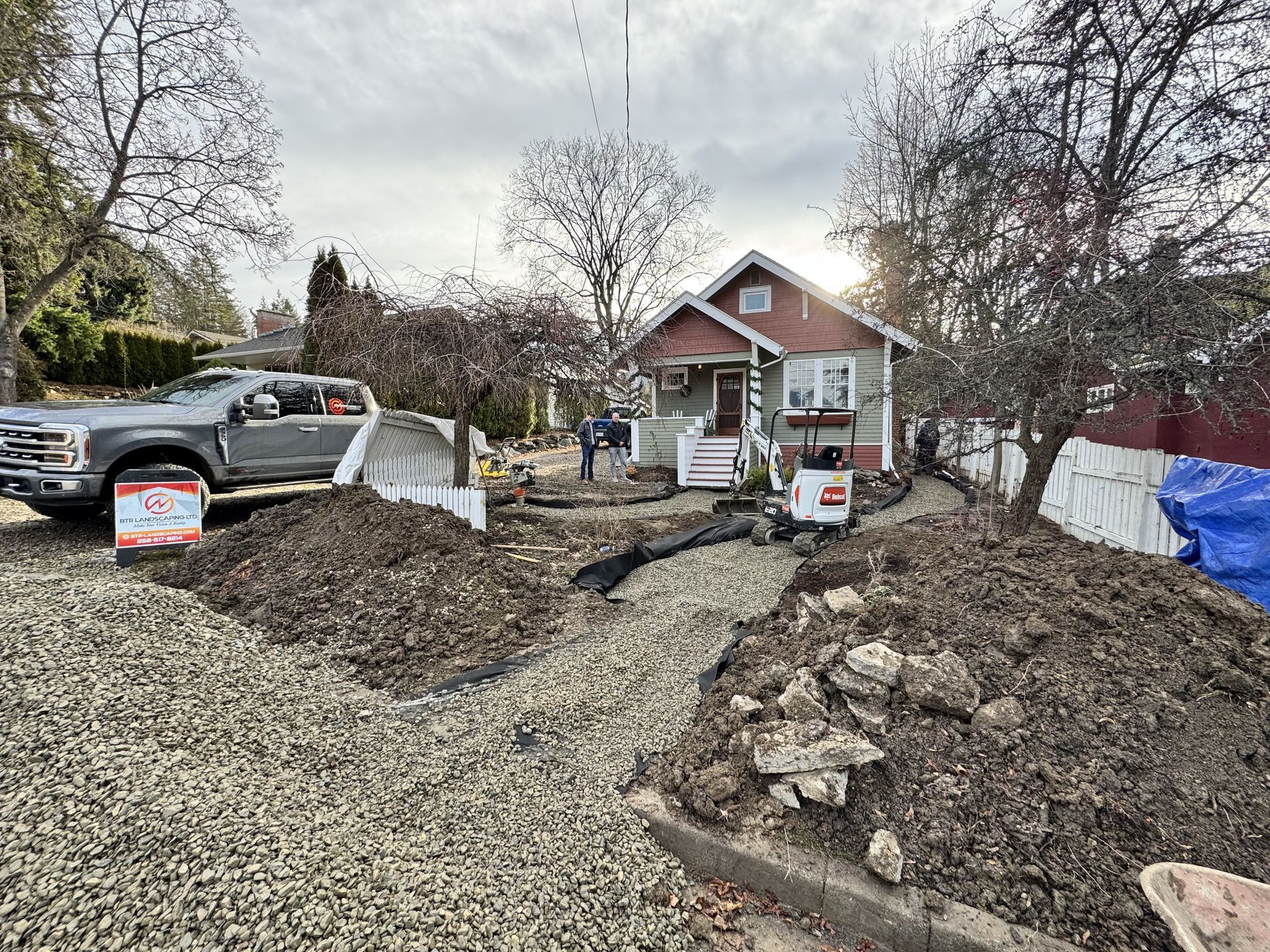 Home under construction with mounds of gravel and dirt in front yard, truck, excavator.