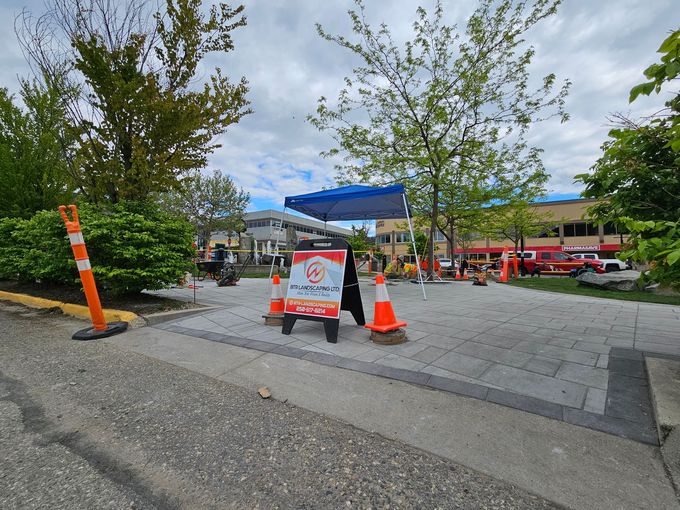 An outdoor event with a sign, cones, and a canopy tent on a brick patio, in front of a building.