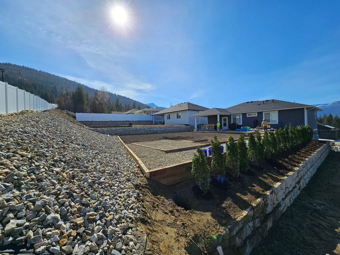 New houses with retaining walls and a rock-covered embankment under a bright blue sky.