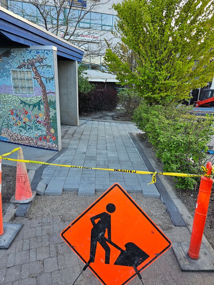 Construction site with orange worker sign and caution tape on brick walkway.