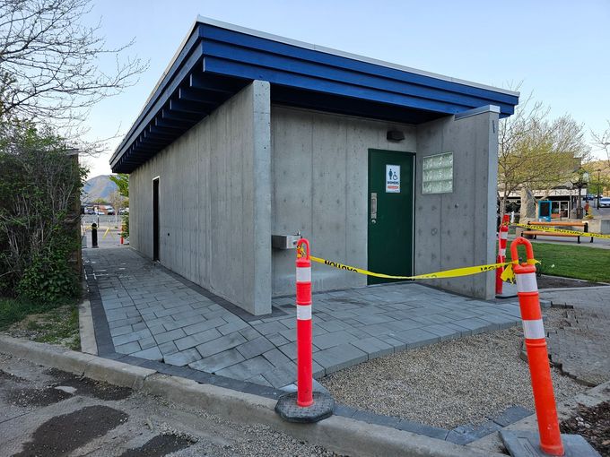 Public restroom building, concrete walls, blue roof trim, green door, caution tape, orange cones.