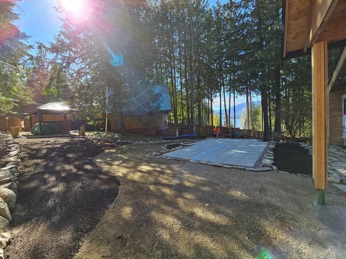 Backyard with gravel, mulch, a structure, and trees on a sunny day.