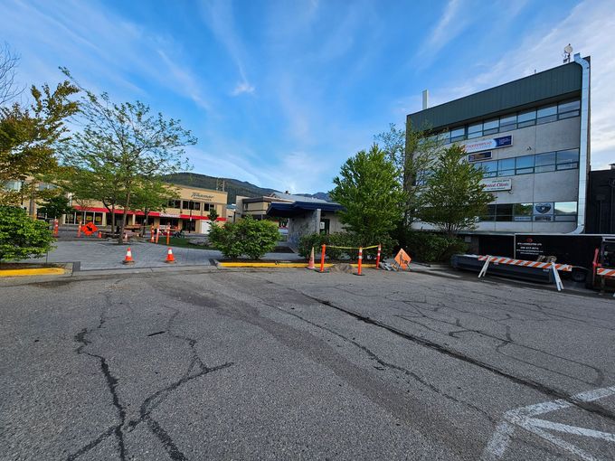 Asphalt parking lot with construction cones, building and trees under a blue sky.