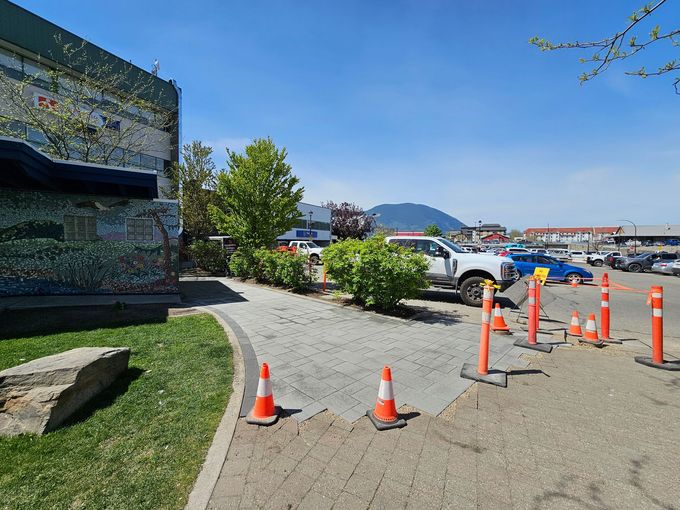 A parking area with orange cones, a white truck, and a building with a mural under a blue sky.