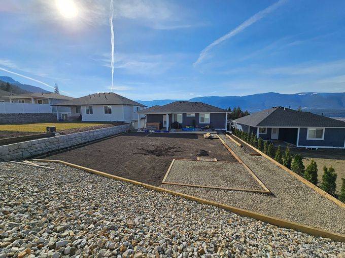 Backyard with newly planted soil, gravel pathway, and blue houses with mountain view.