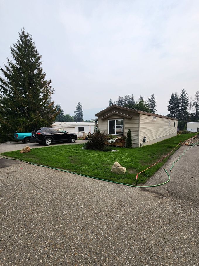 Mobile home with small lawn, car parked on the side, driveway, and green hose on a cloudy day.