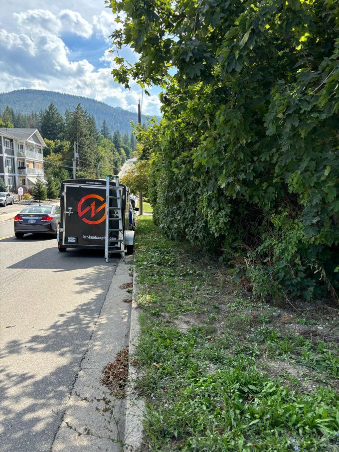A trailer parked by a roadside, with a green area and a hill in the background.