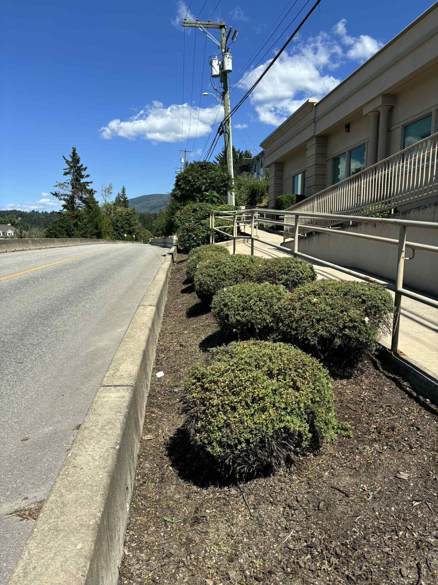 Roadside view of a building with a ramp, bushes, and power lines against a blue sky.