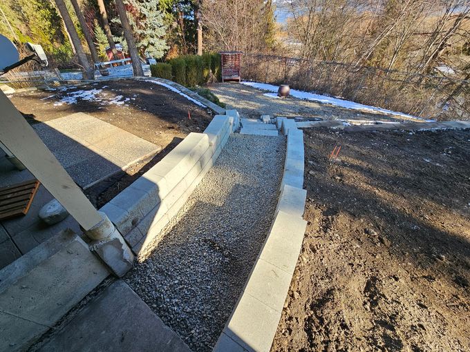Stone steps and gravel path between concrete retaining walls on a hillside.