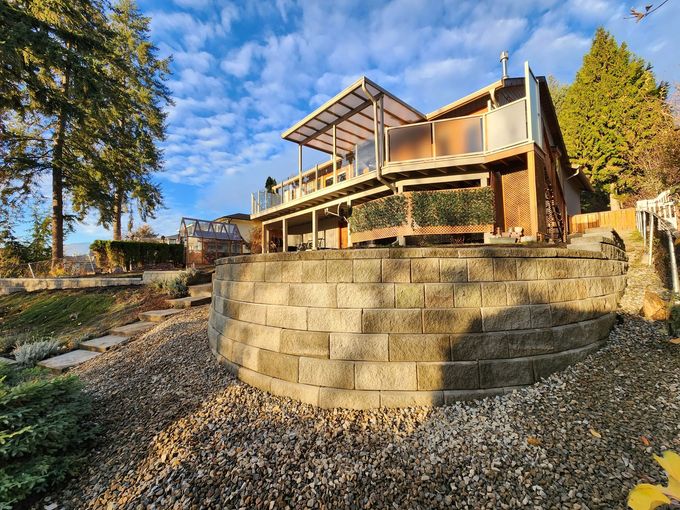 House with a deck overlooking a retaining wall and a landscaped yard on a sunny day.