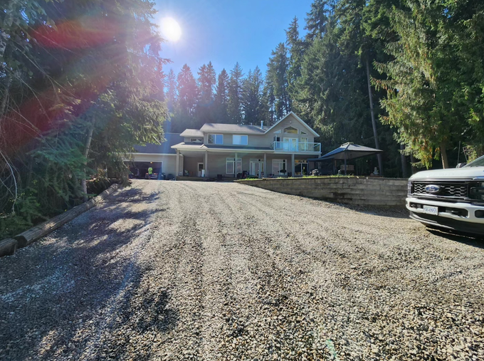 A large house with a gravel driveway, forest backdrop, and a parked white truck.