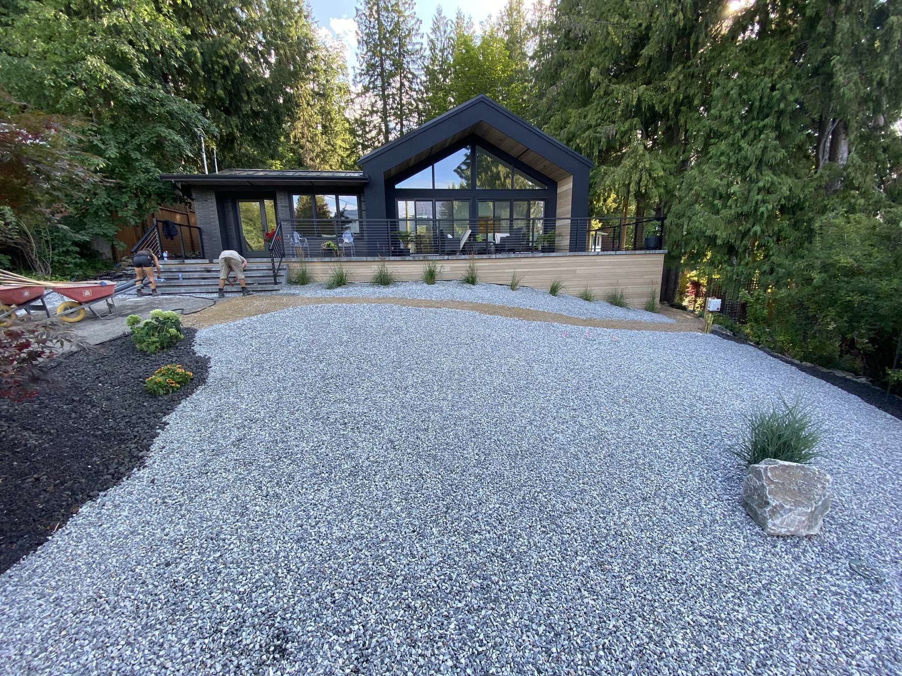 Modern house with large windows, grey gravel driveway, and landscaping.