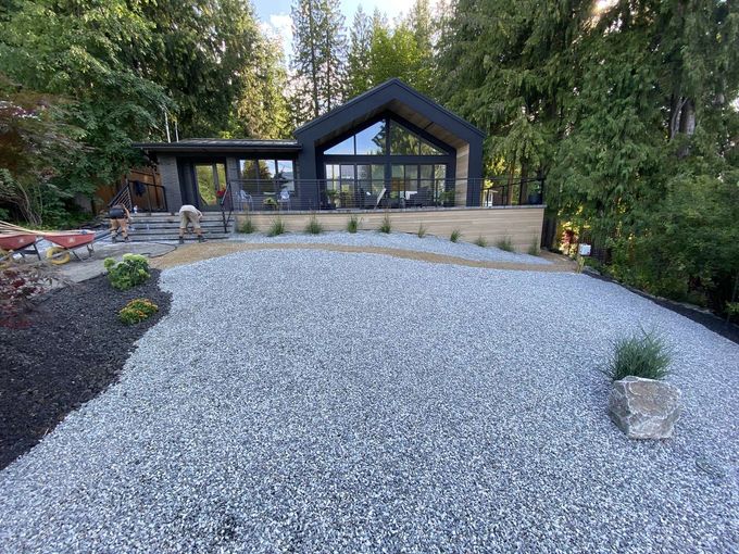 Modern house with large windows, grey gravel driveway, and landscaping.