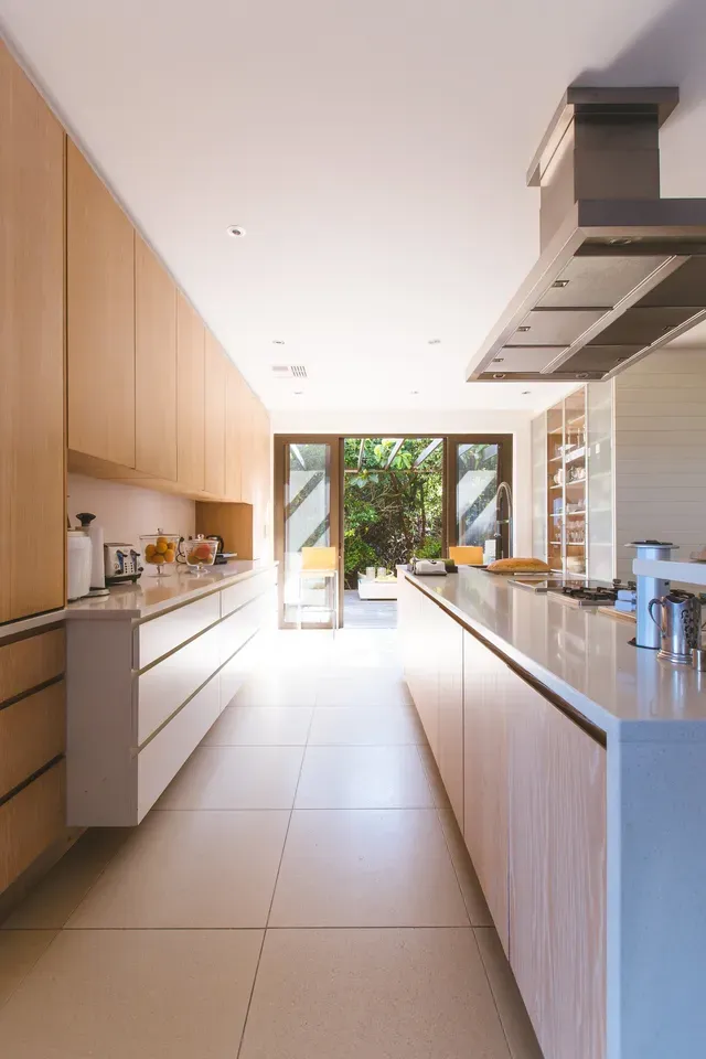 Modern kitchen with light wood cabinets, white countertops, and large glass doors.