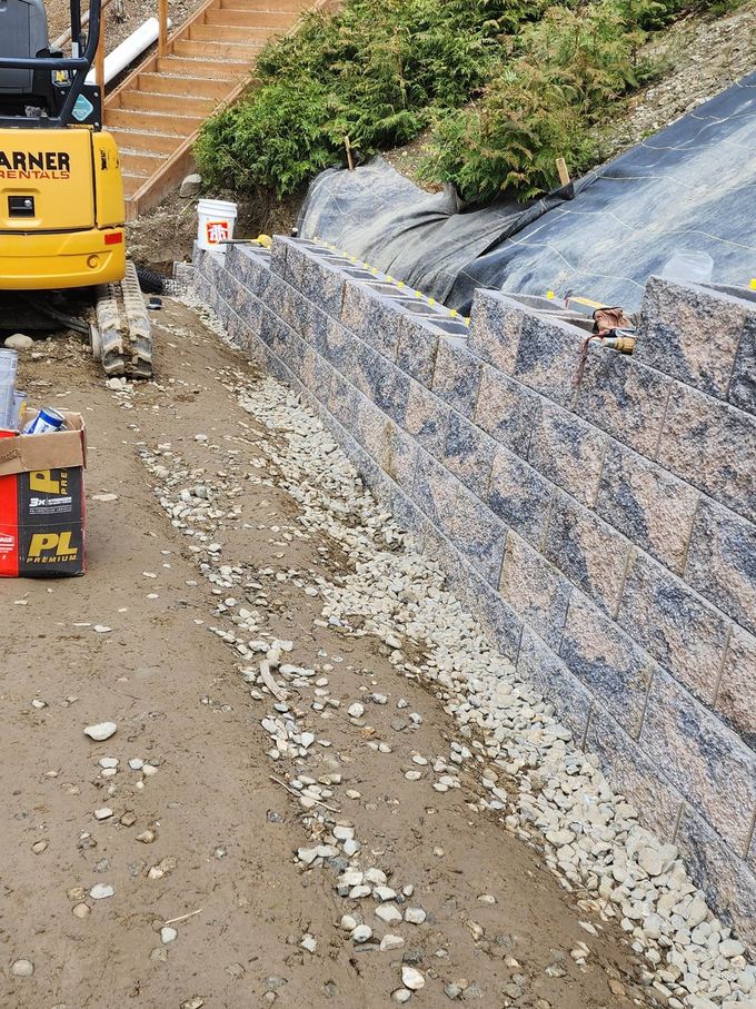 Construction site with a retaining wall being built, with an excavator and materials.