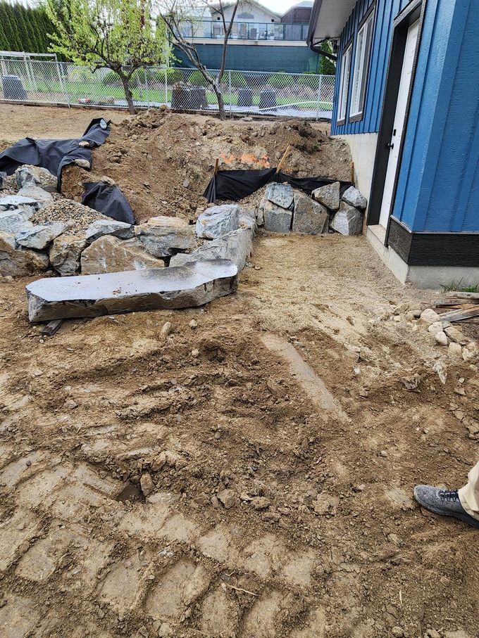 Construction site with large rocks, dirt, and a blue building.
