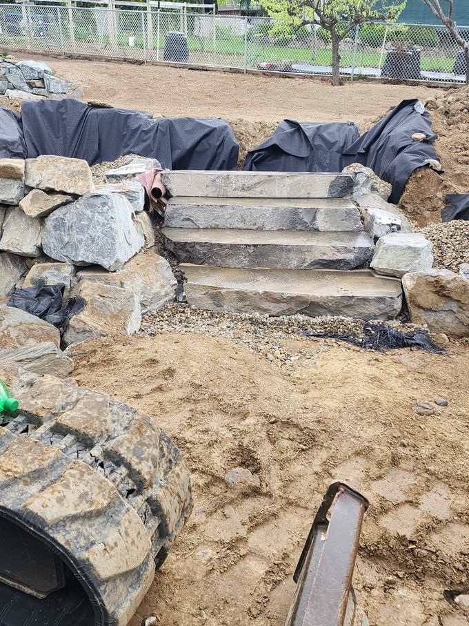 A partially built outdoor staircase made of concrete steps and stone retaining walls, in a muddy environment.