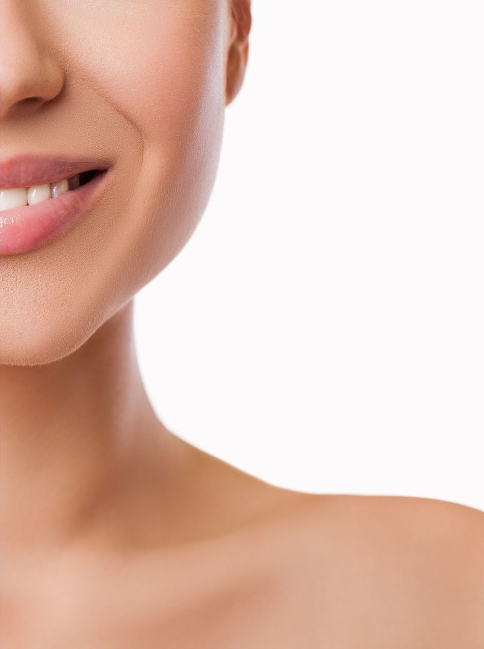 Smiling woman's face and bare shoulder, showing healthy skin and white teeth against a white background.
