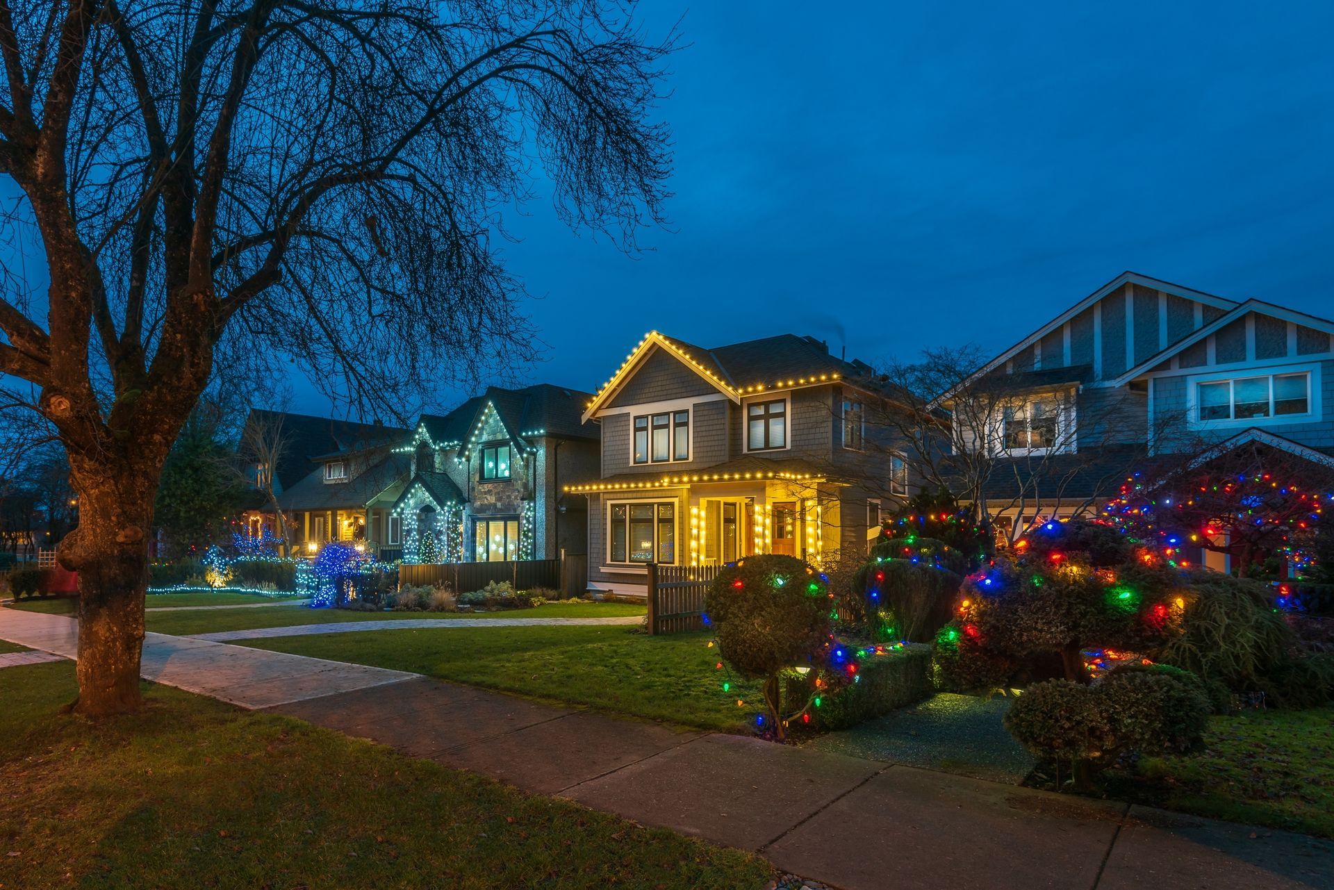 Houses decorated with colorful Christmas lights at dusk.