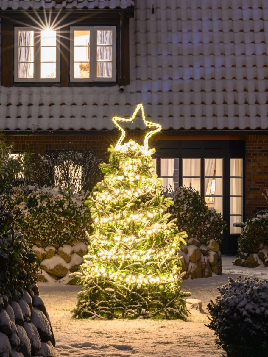 Snowy house exterior with illuminated Christmas tree and star topper.
