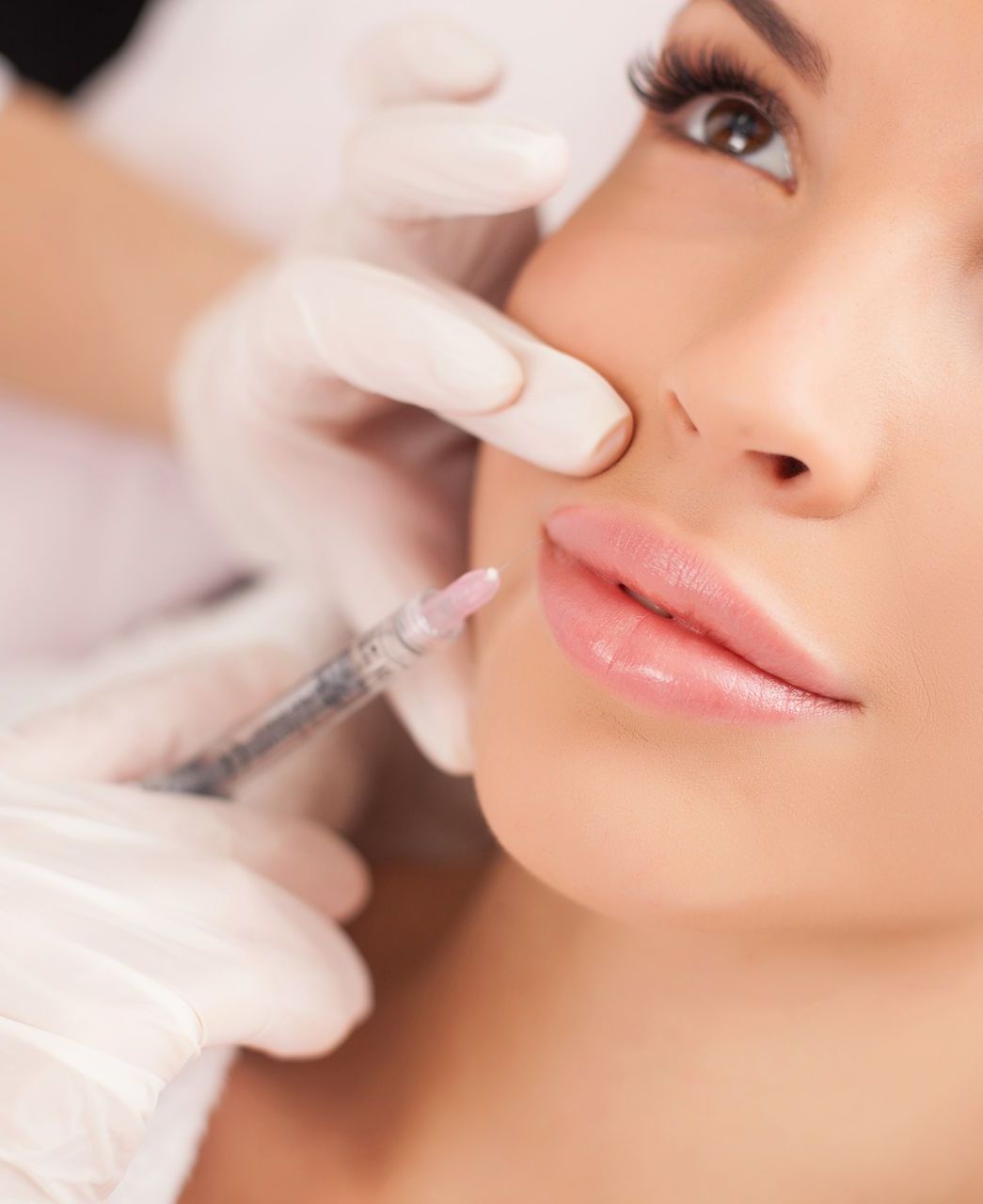 Woman receiving lip filler injection; gloved hands, close-up view, beauty treatment.