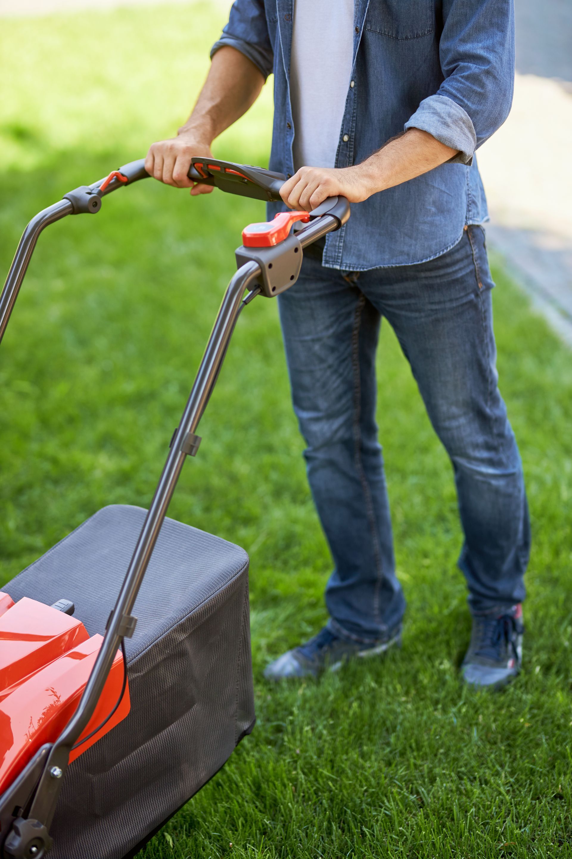 Man mowing green grass with a red and black lawnmower.