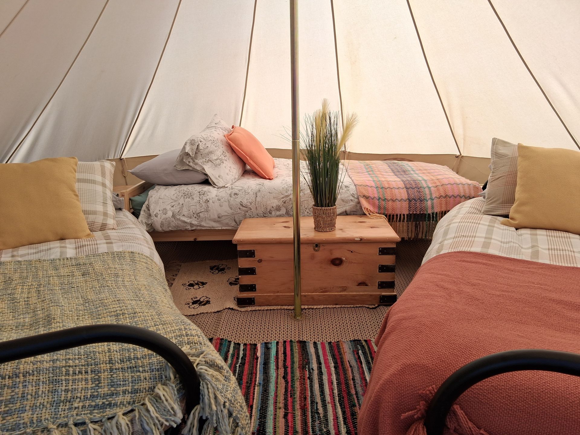 Glamping tent lit at dusk, furnished with beds, rugs, and string lights, set in a field.