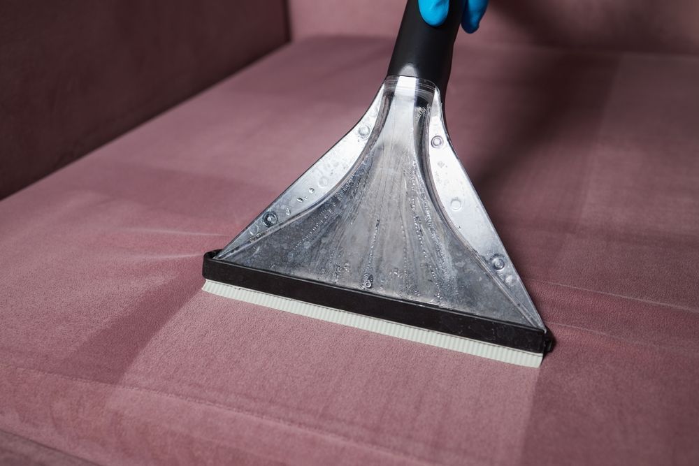 A Person is Cleaning a Pink Couch With a Vacuum Cleaner — We Clean Lounges In Caloundra, QLD