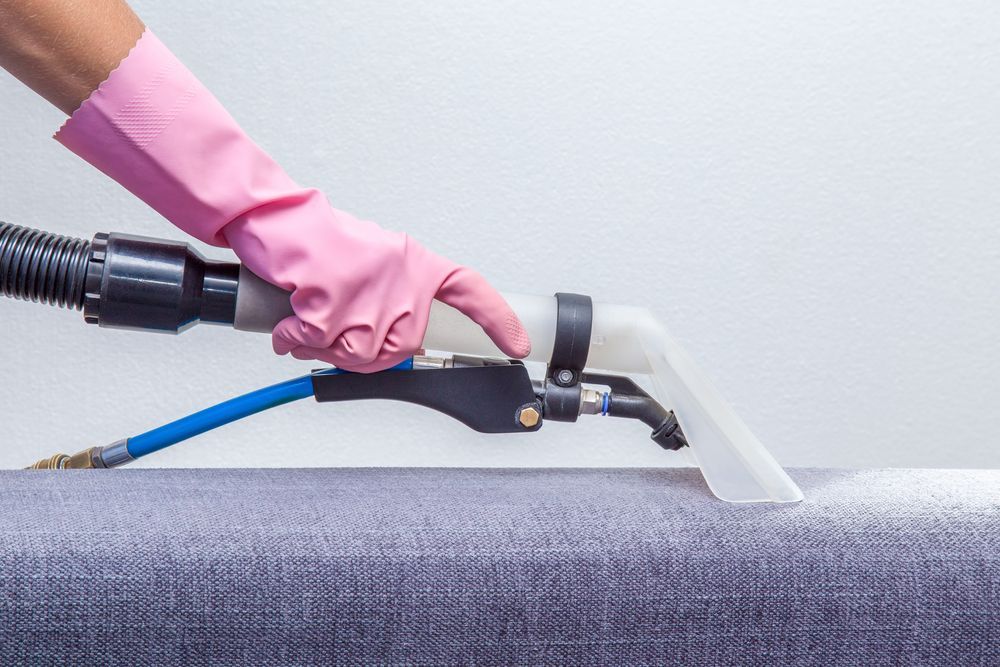 A Person With Pink Gloves is Cleaning a Gray Couch — We Clean Lounges In Bli Bli, QLD